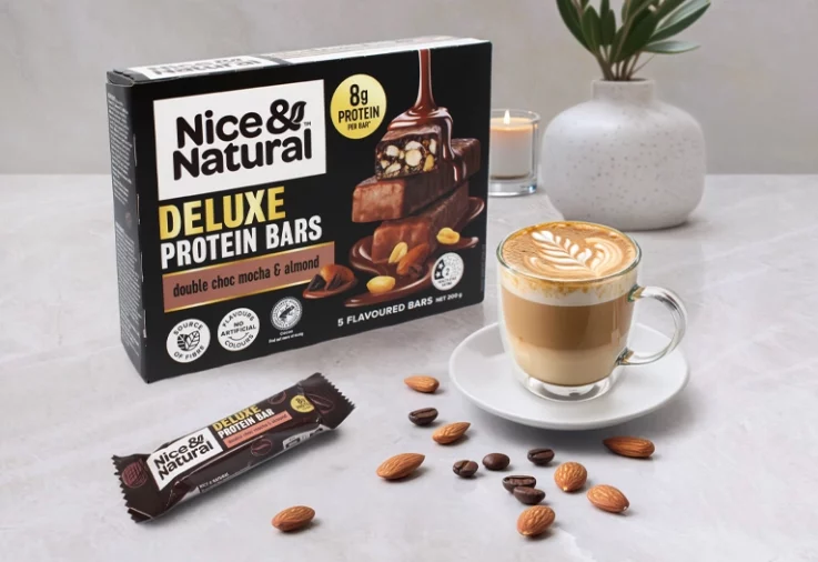 Nice and Natural Deluxe Protein Bars in mocha flavour next to a cup of coffee and some nuts.